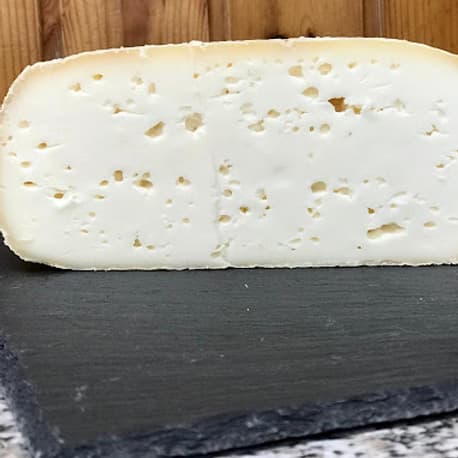 Una caciotta senza lattosio tagliata, dalla pasta bianca con piccoli occhi, su una lastra di ardesia