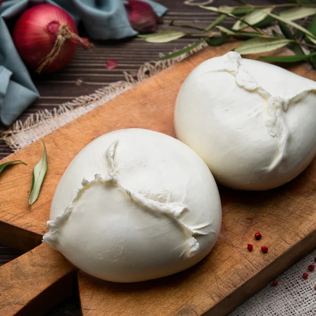 Due mozzarelle di bufala Sdino su un tagliere di legno, con pomodorini e foglie