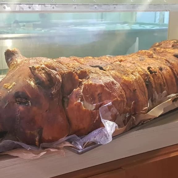 Una porchetta di Ariccia intera, dalla cotenna dorata, sul banco