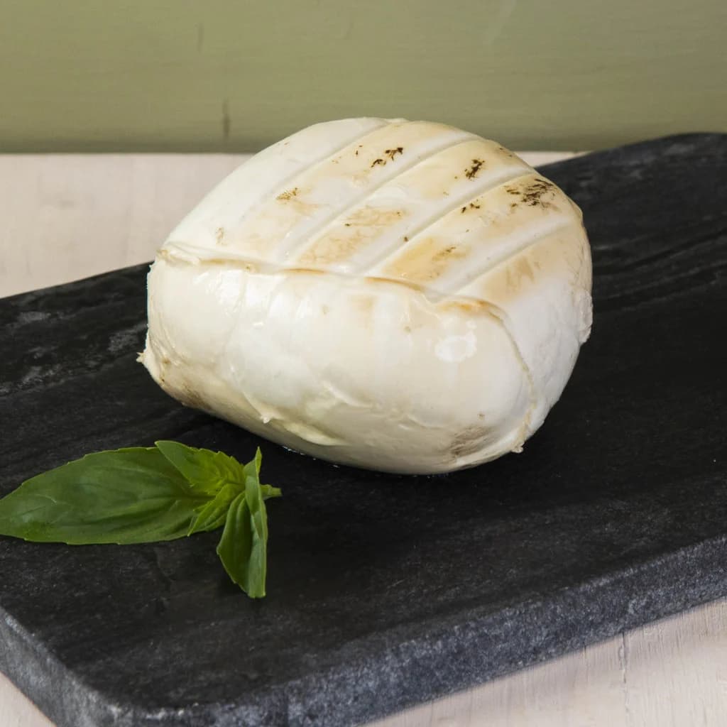 Una provola di bufala affumicata, dalla buccia dorata, su una lastra di ardesia con basilico